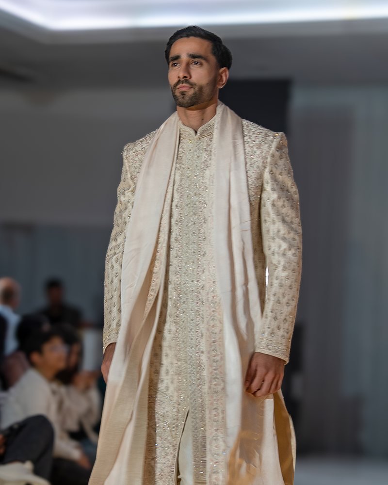 A model in a cream embroidered sherwani with a draped shawl on the runway