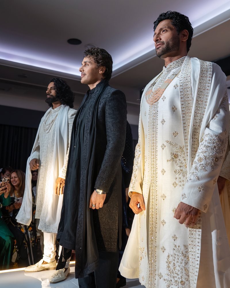 Three models in ivory and black sherwanis lined up under the runway lights